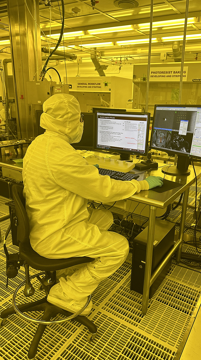 A person wearing a protective suit works in a laboratory bathed in yellow light.