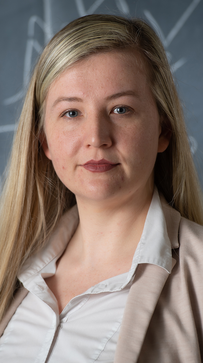 Headshot of a woman wearing a tan jacket over a white blouse.