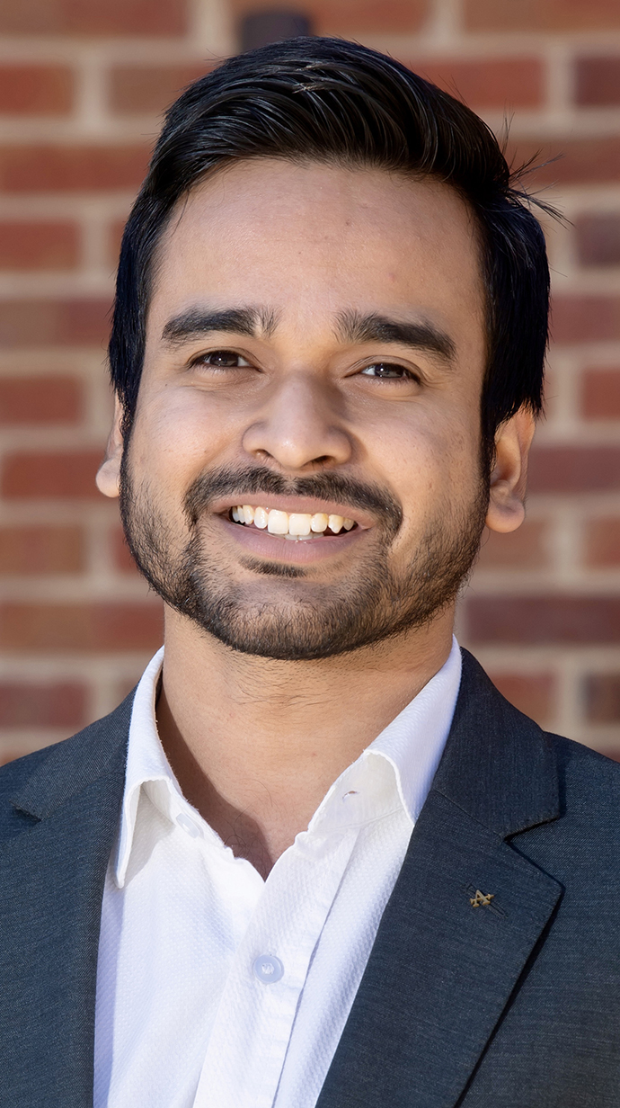 Headshot of a man wearing a dark blue jacket over an open-collared white dress shirt.