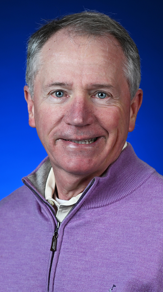 Headshot of a man wearing a lilac zippered sweatshirt over a white shirt.