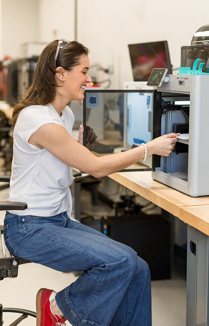 A young woman takes a finished piece out of a 3D printer.