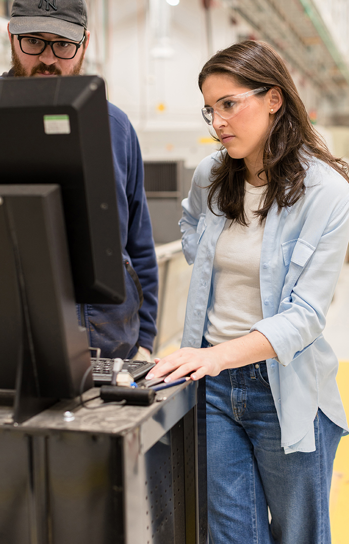 A man and a young woman work with a piece of equipment in a machine shop.