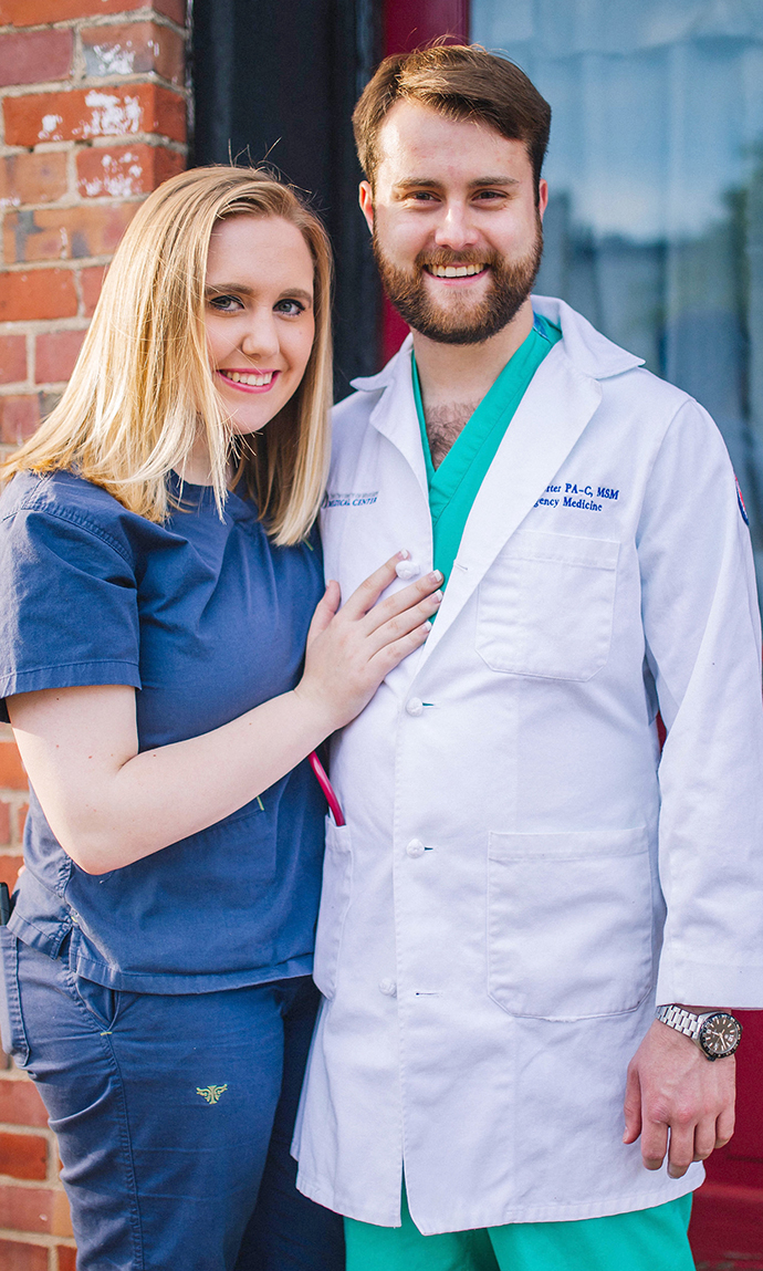 A man and a woman, both wearing medical scrubs, stand outside a brick building.