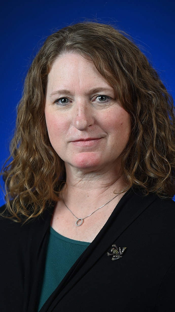 Headshot of a woman wearing a black jacket over a green blouse.