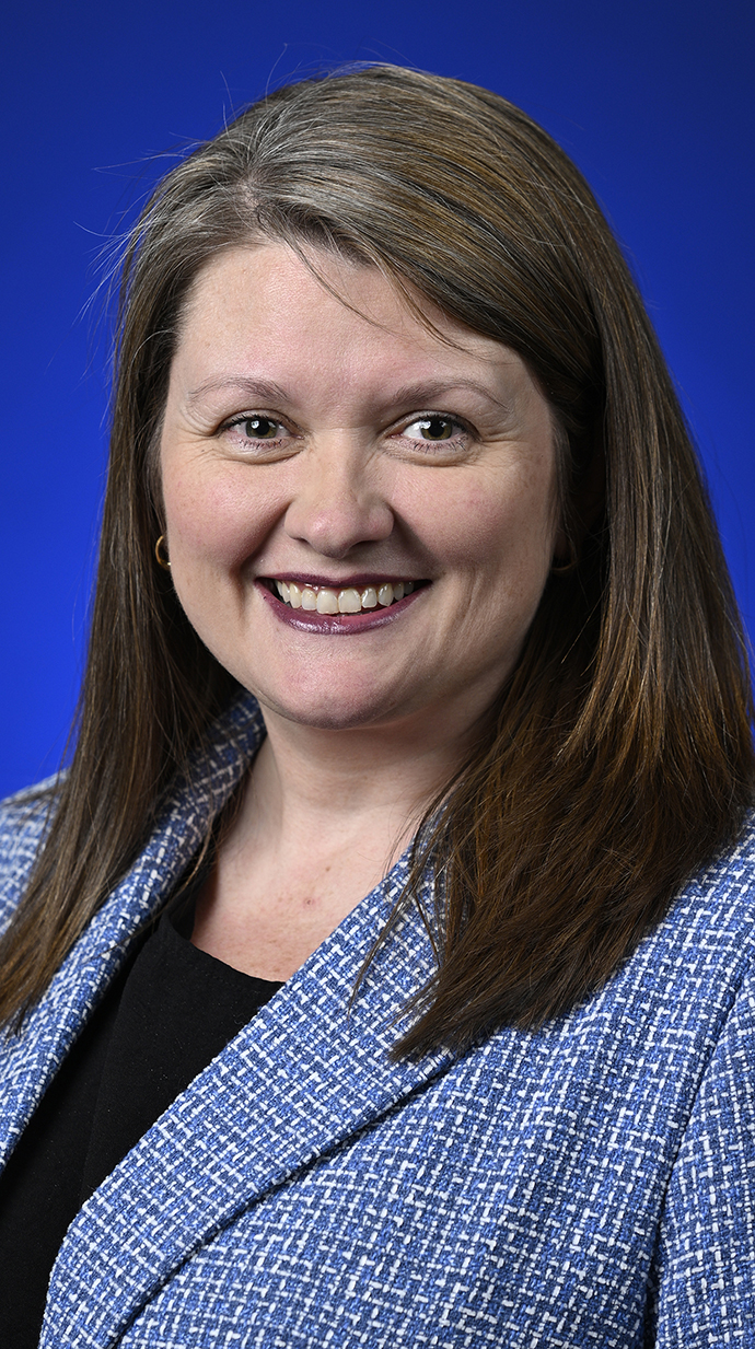 Headshot of a woman wearing a blue jacket over a black blouse.