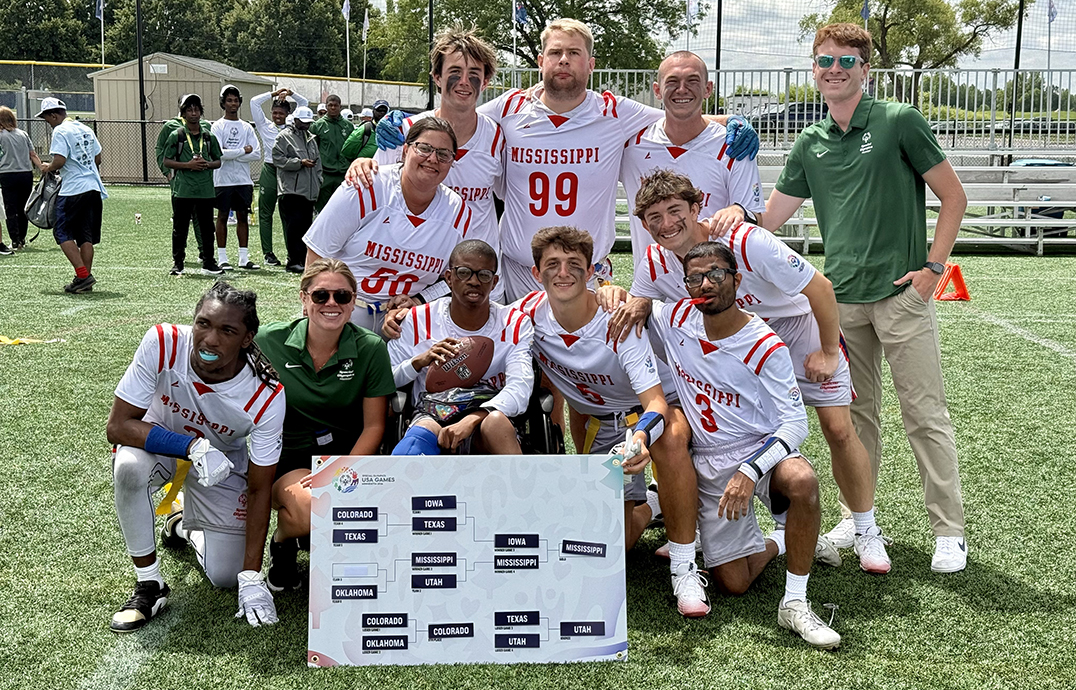 A football team gathers on a field with a schedule bracket in front of them.