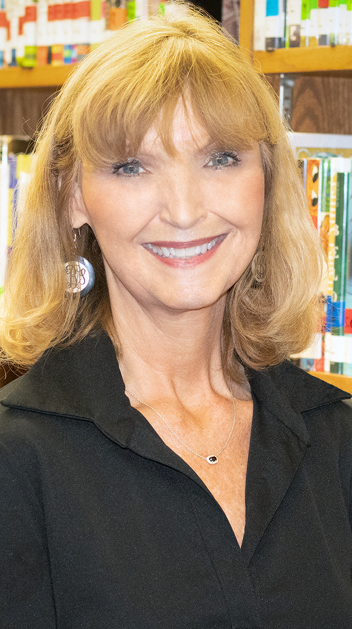 Headshot of a woman wearing a black blouse standing in front of filled bookshelves.