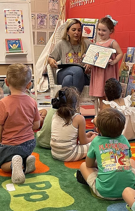 A women reads a picture book to children seated on the floor of a classroom.