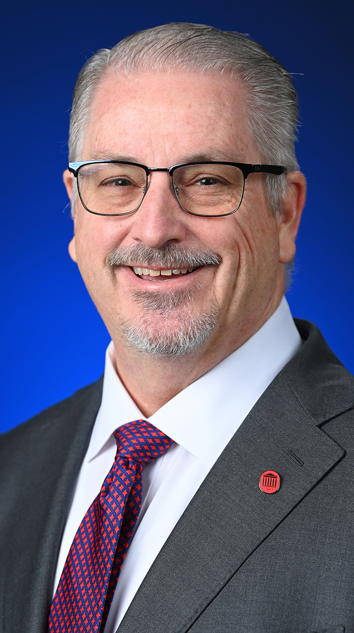 Headshot of a man wearing glasses and a gray suit.