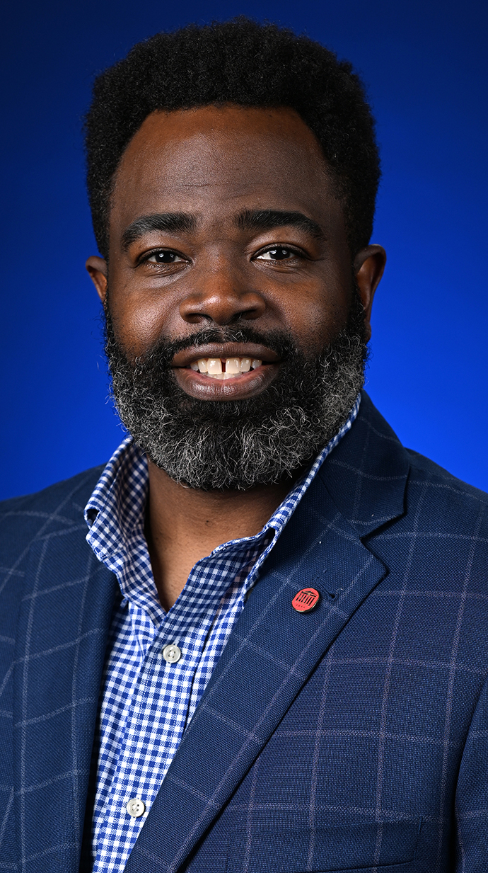Headshot of a man wearing a dark blue jacket over a blue checked shirt.