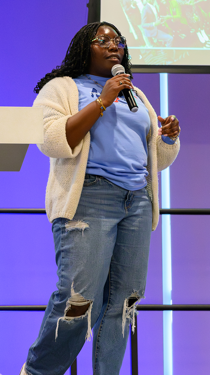 A young woman speaks from the front of a conference room.