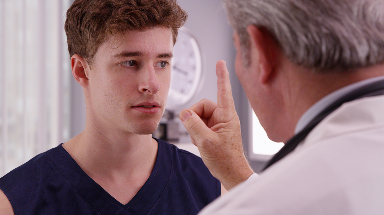 A doctor has a young man follow a finger with his eyes to check for concussion.