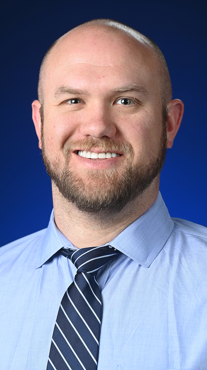 Headshot of a man wearing a blue dress shirt with a dark blue tie.