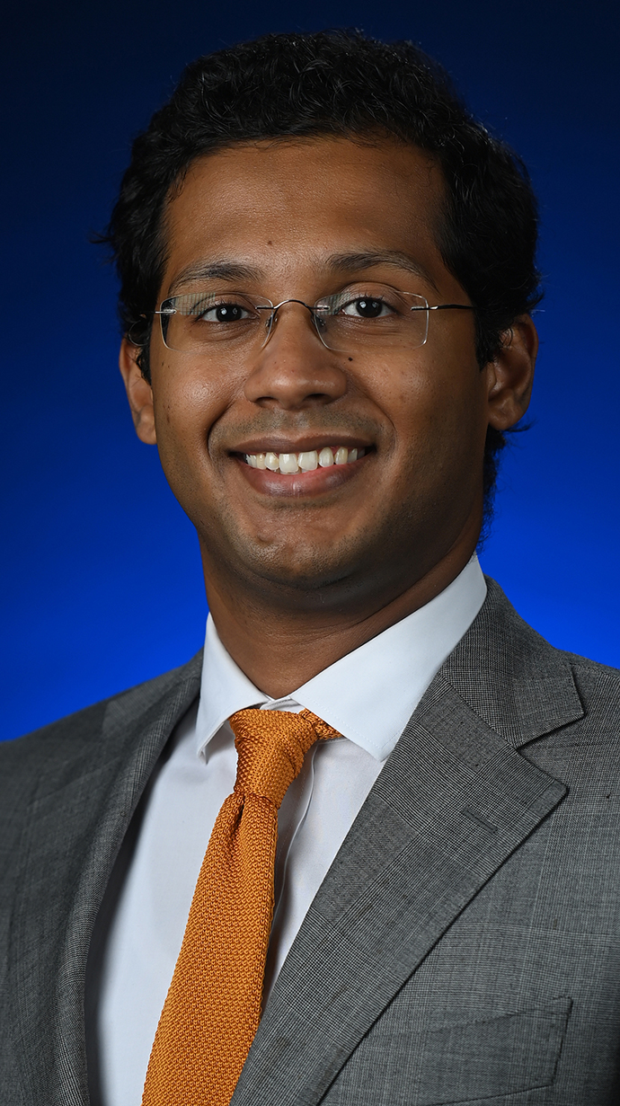 Headshot of a man wearing a brown suit with an orange tie.