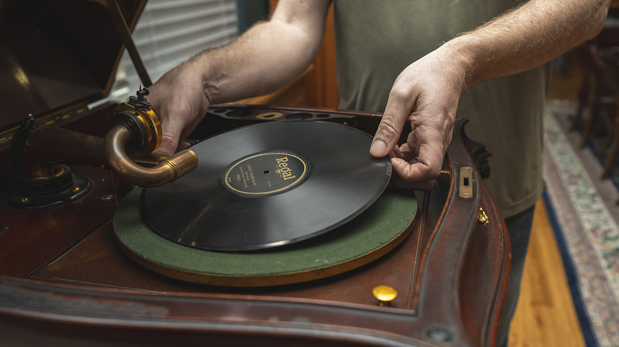 A hand places a vinyl LP on the turntable of a vintage phonograph.