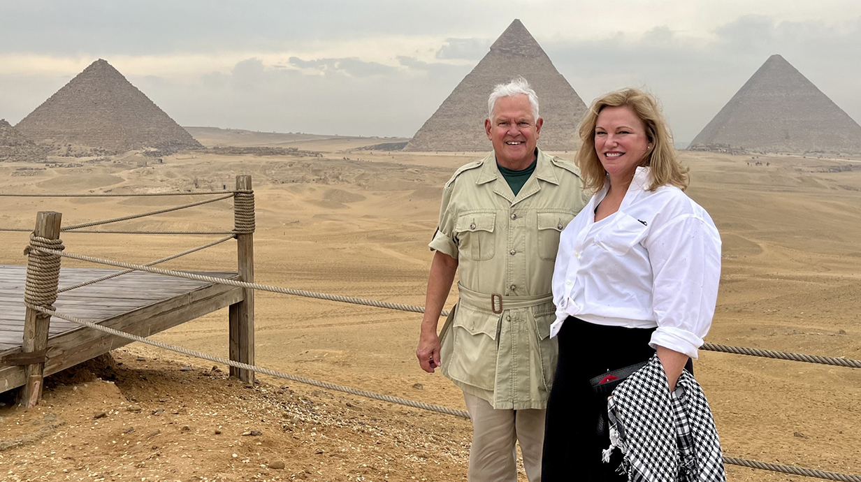 A man and a woman stand in front of the great pyramids in Egypt.