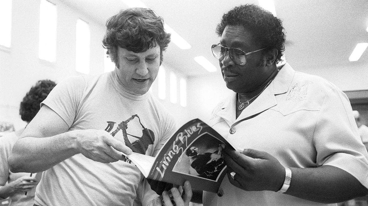 Black-and-white photograph of two men looking at a magazine titled Living Blues.