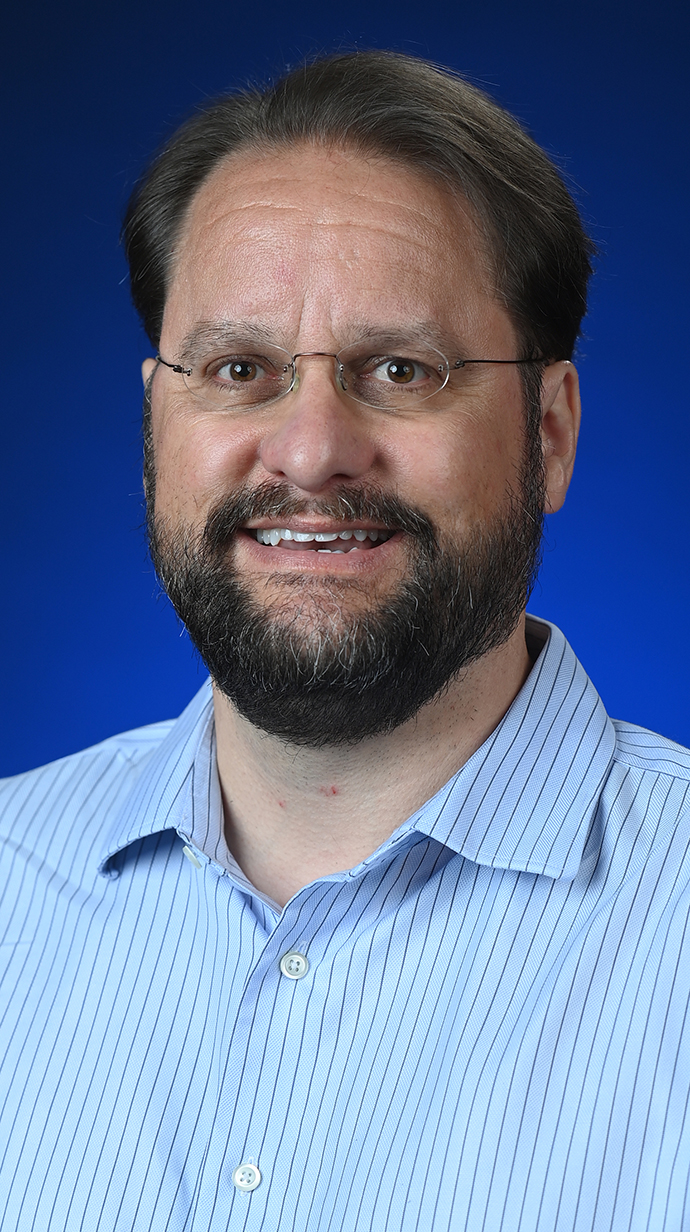 Headshot of a man wearing an open-collared blue dress shirt.