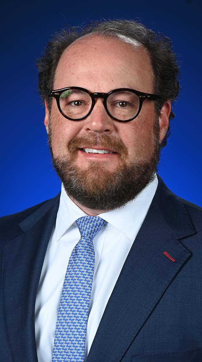 Headshot of a man wearing a dark suit with a light blue tie.