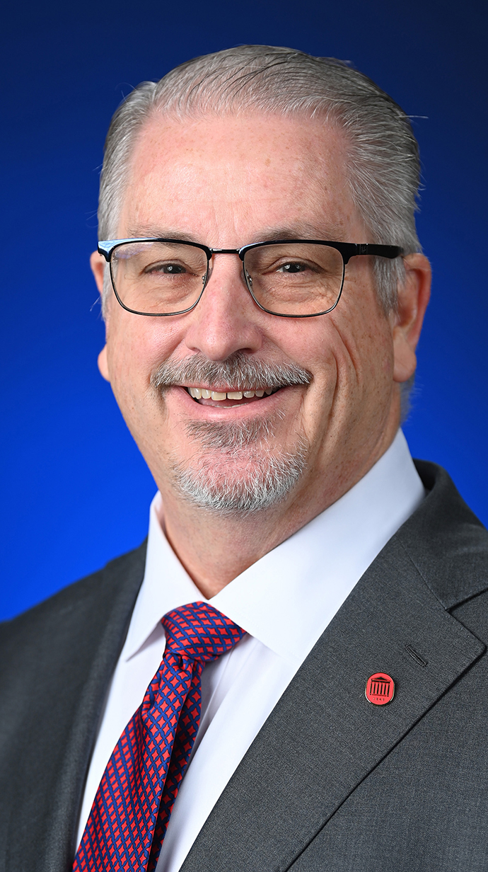 Headshot of a man wearing a gray suit with a purple tie.