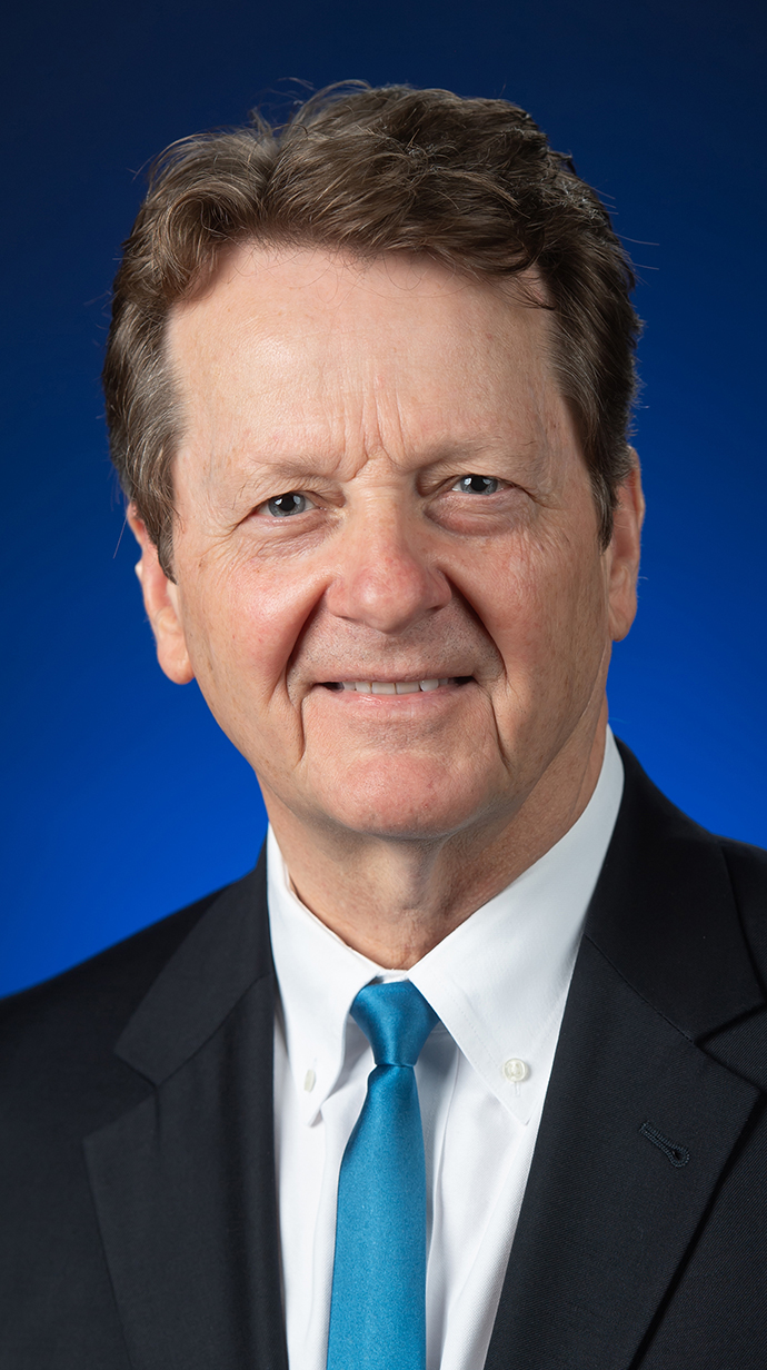 Headshot of a man wearing a dark suit with a blue-green tie.