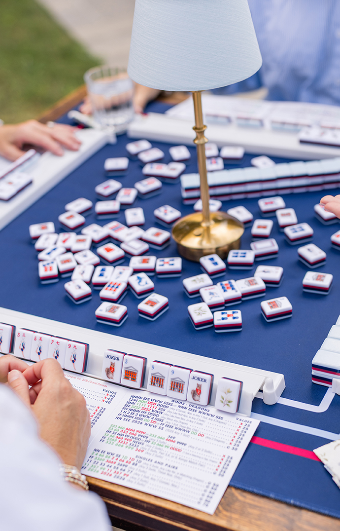 Mahjong tiles and cards line a table topped with a blue mat.
