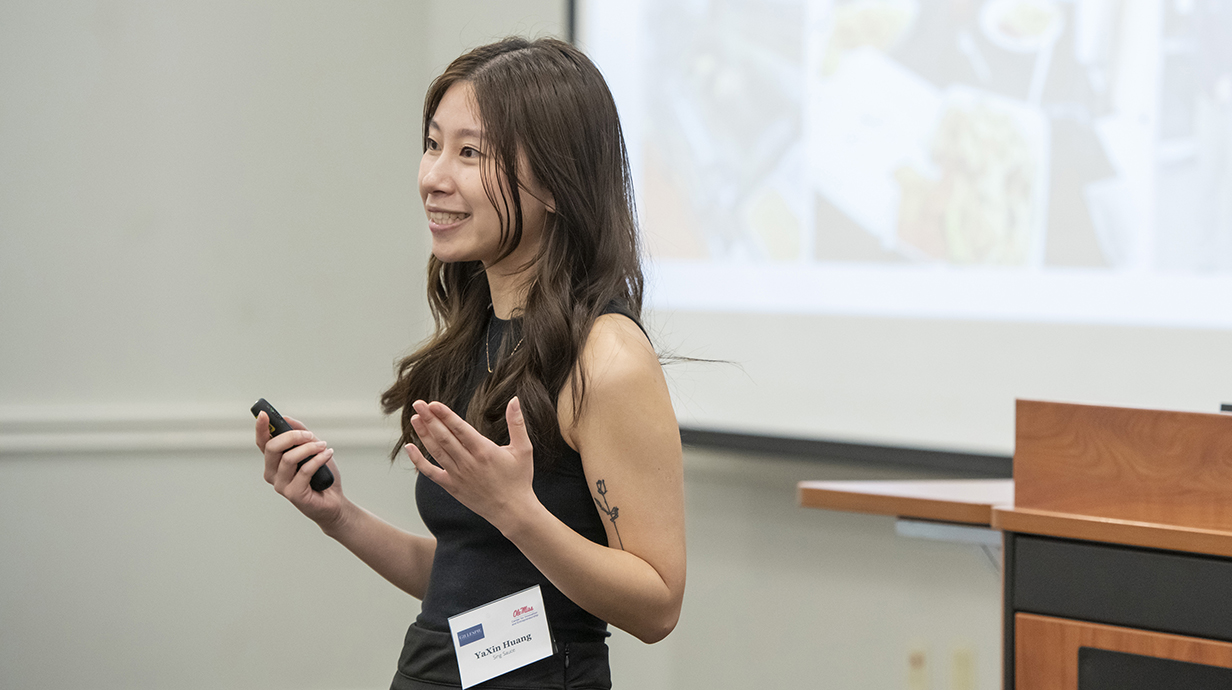 A young woman speaks at the front of a classroom.