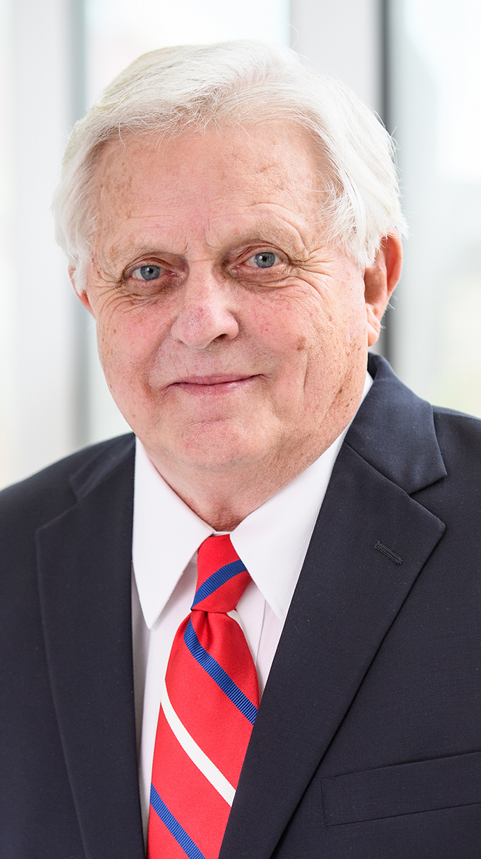 Headshot of a man wearing a dark suit and a red striped tie.