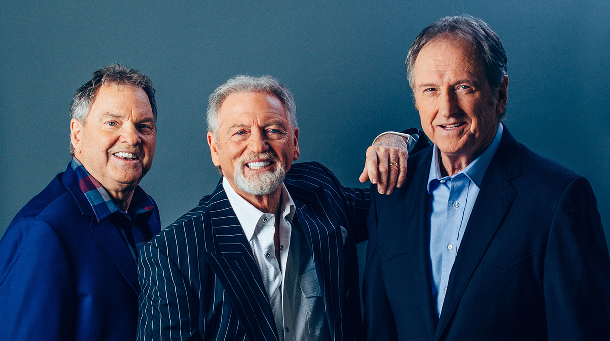 Three men wearing blue jackets pose for a publicity photo.