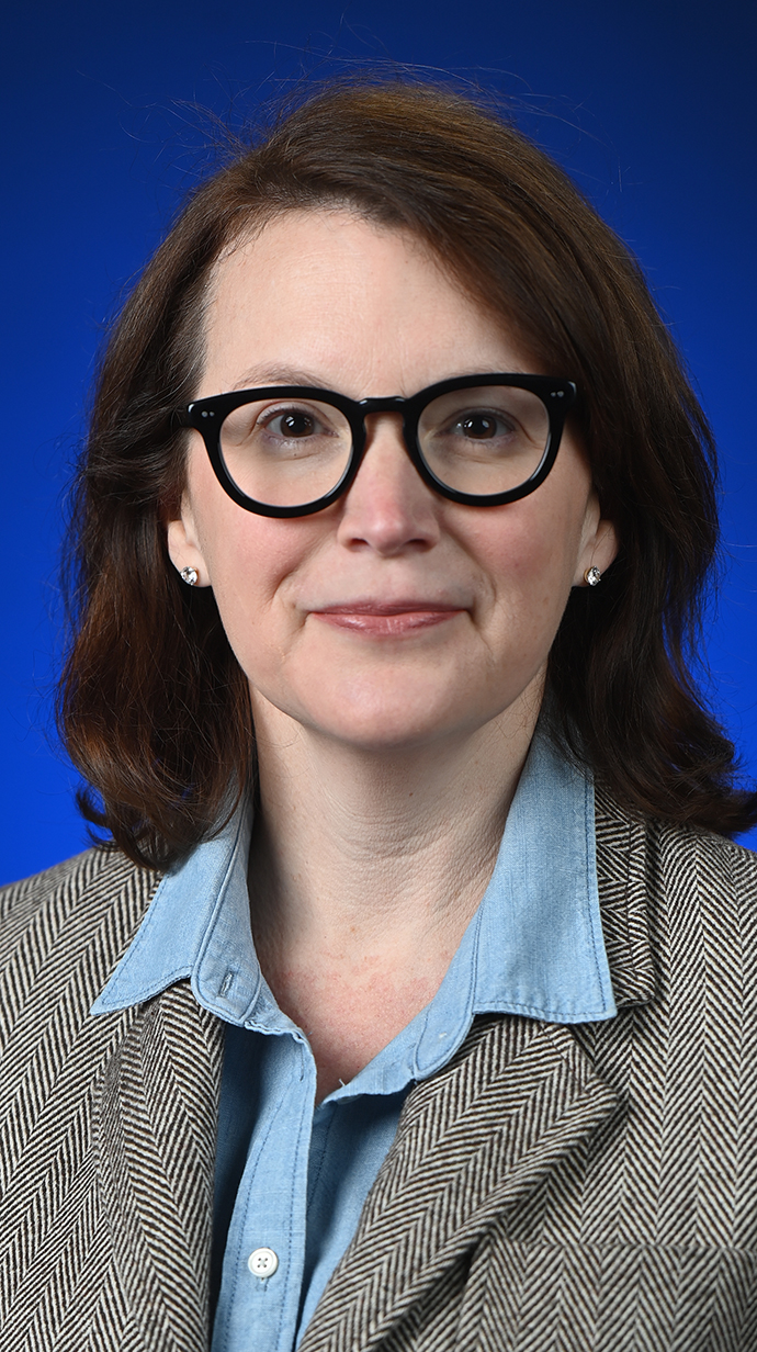 Headshot of a woman wearing a tweed jacket over a light blue shirt.