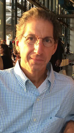 Headshot of a man sitting in a sunny atrium.