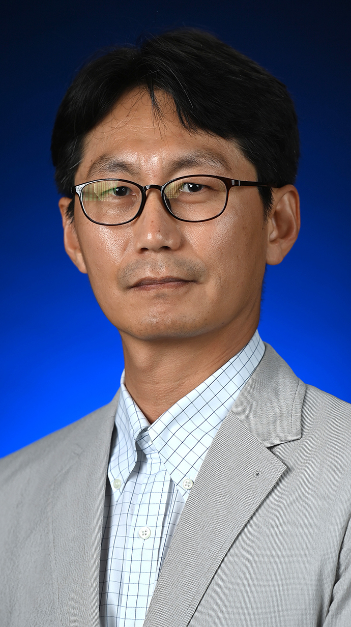 Headshot of a man wearing a gray jacket over a white shirt with a blue windowpane check.