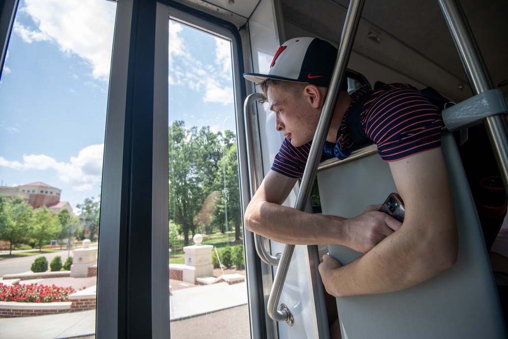 Young man leans out the window of a bus, looking down.