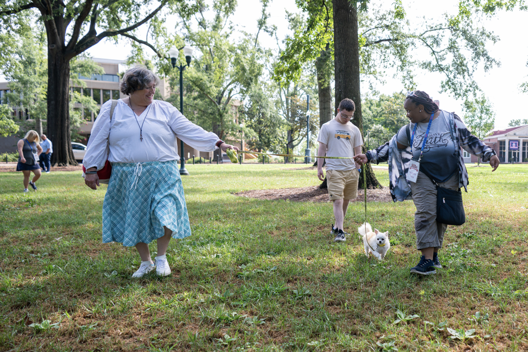 Young woman holds a dog's leash while walking with an older woman through a grove of trees.