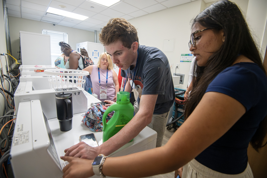 Woman helps a young man operate a washing machine in a laundry room.