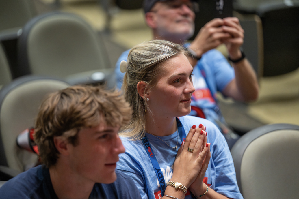 Two people watch students rehearse dance choreography in a room.