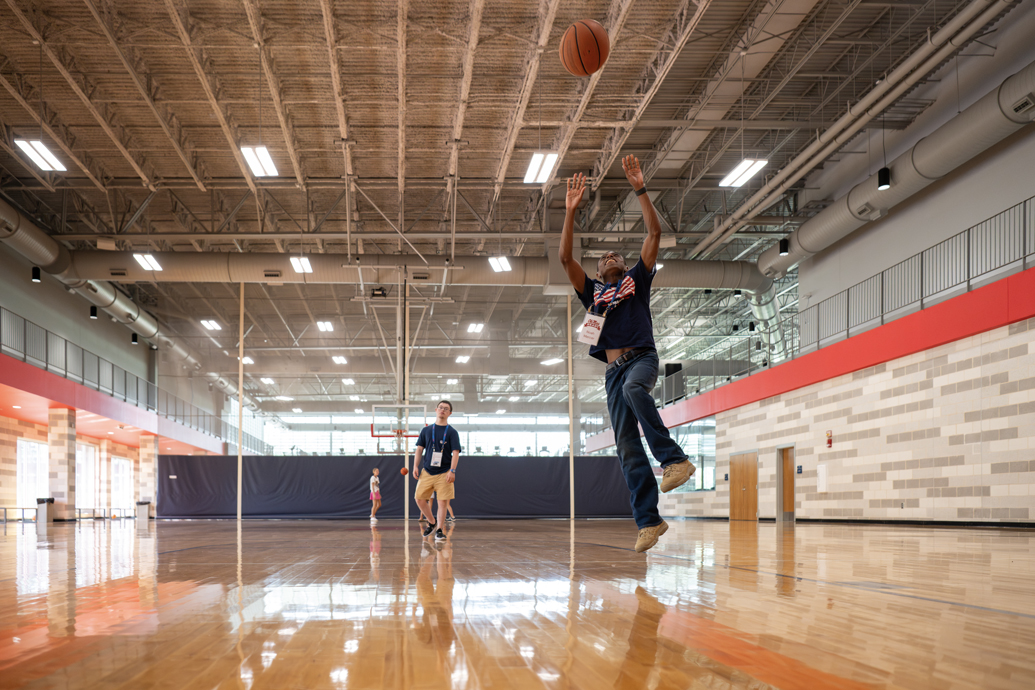 Two young men play basketball in an empty gymnasium.