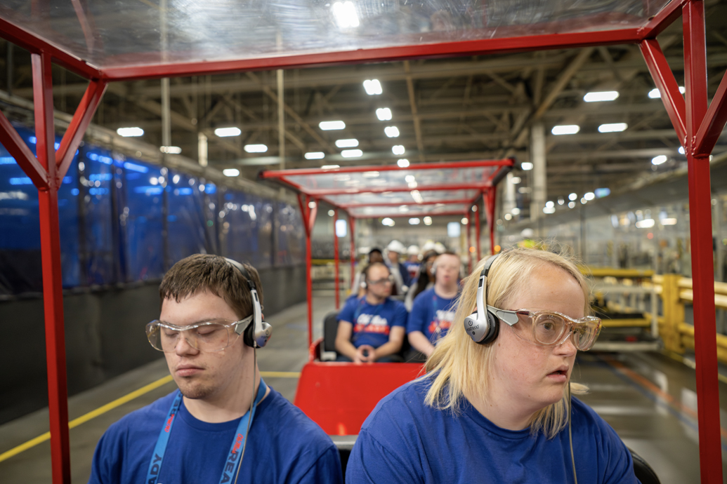 Two students wearing safety glasses and headphones tour a manufacturing facility.