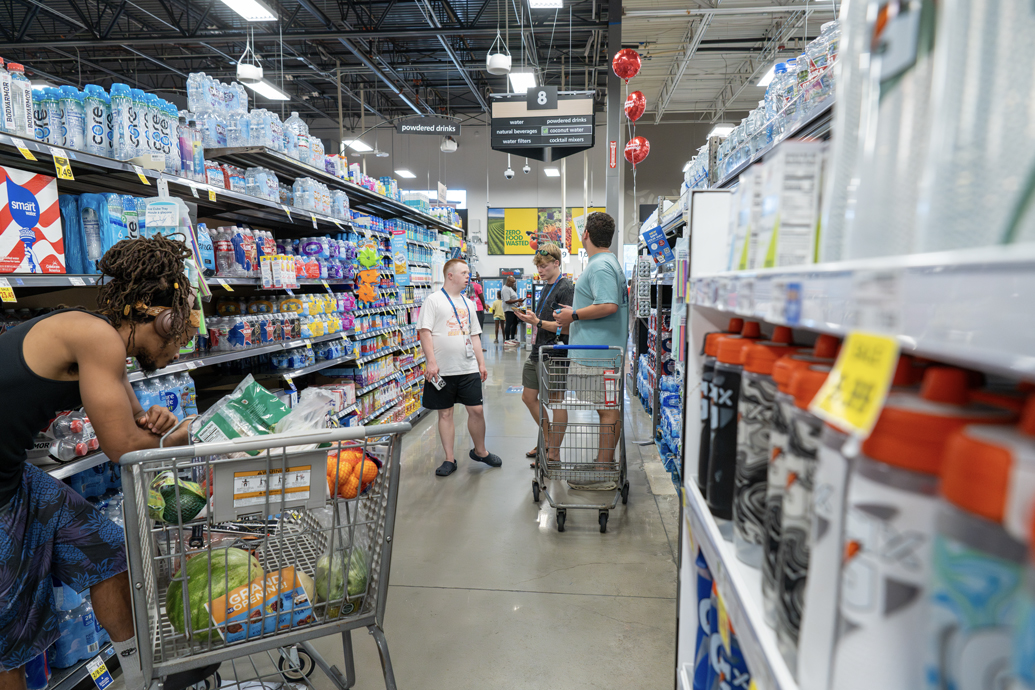 Young man shops for groceries with two mentors in a store aisle.