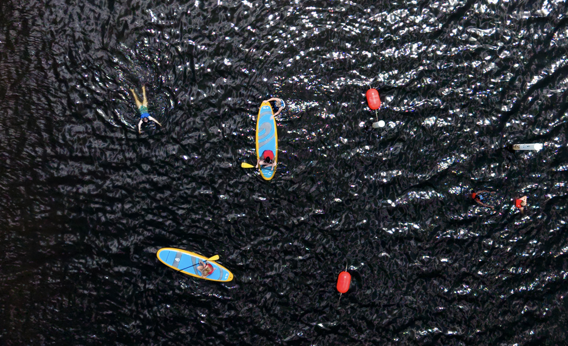 Aerial view of students paddleboarding and swimming on a lake.