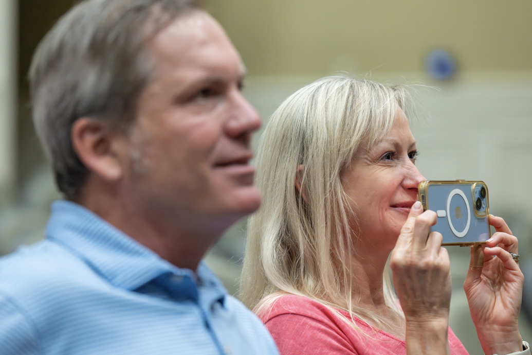 Man and woman sit in an audience, smiling.