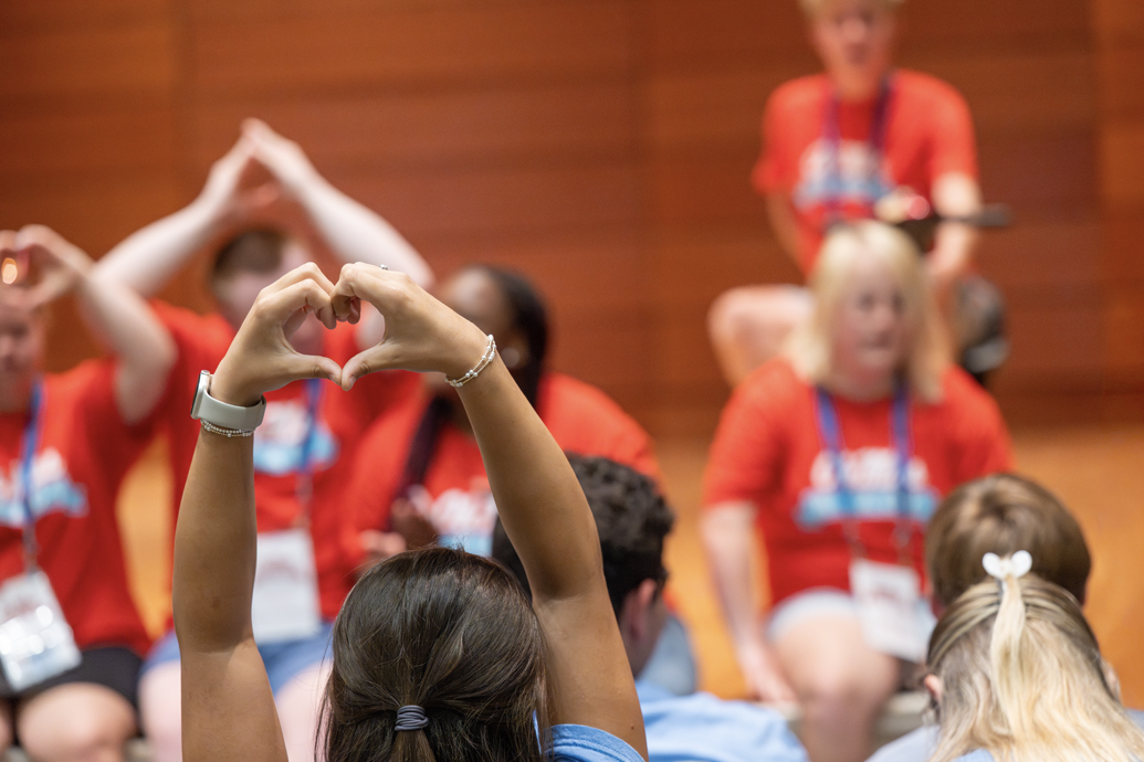 Woman holds her hands in a heart shape near a stage.