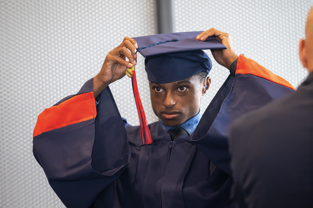 Young man in a cap and gown adjusts his graduation cap.