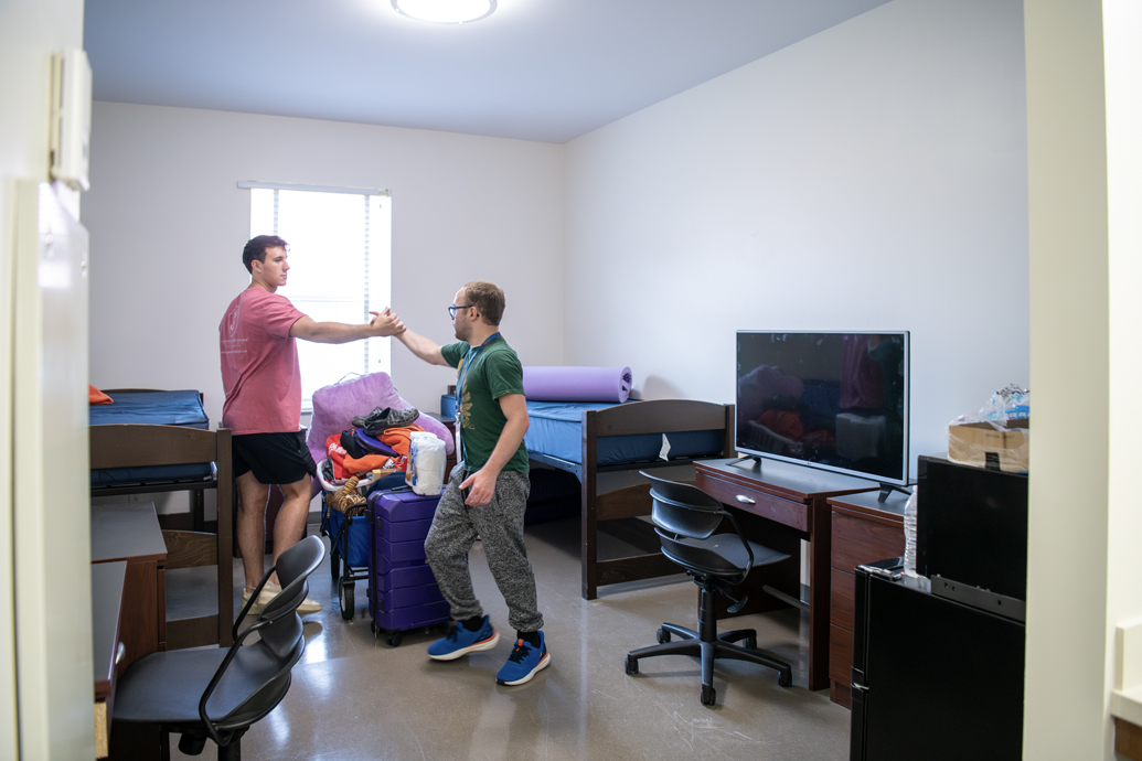 Two men high-five each other beside packed boxes and belongings.