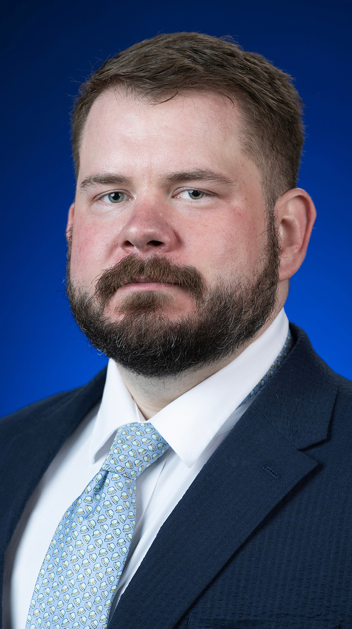 Headshot of a man wearing a dark blue suit and a light blue tie.