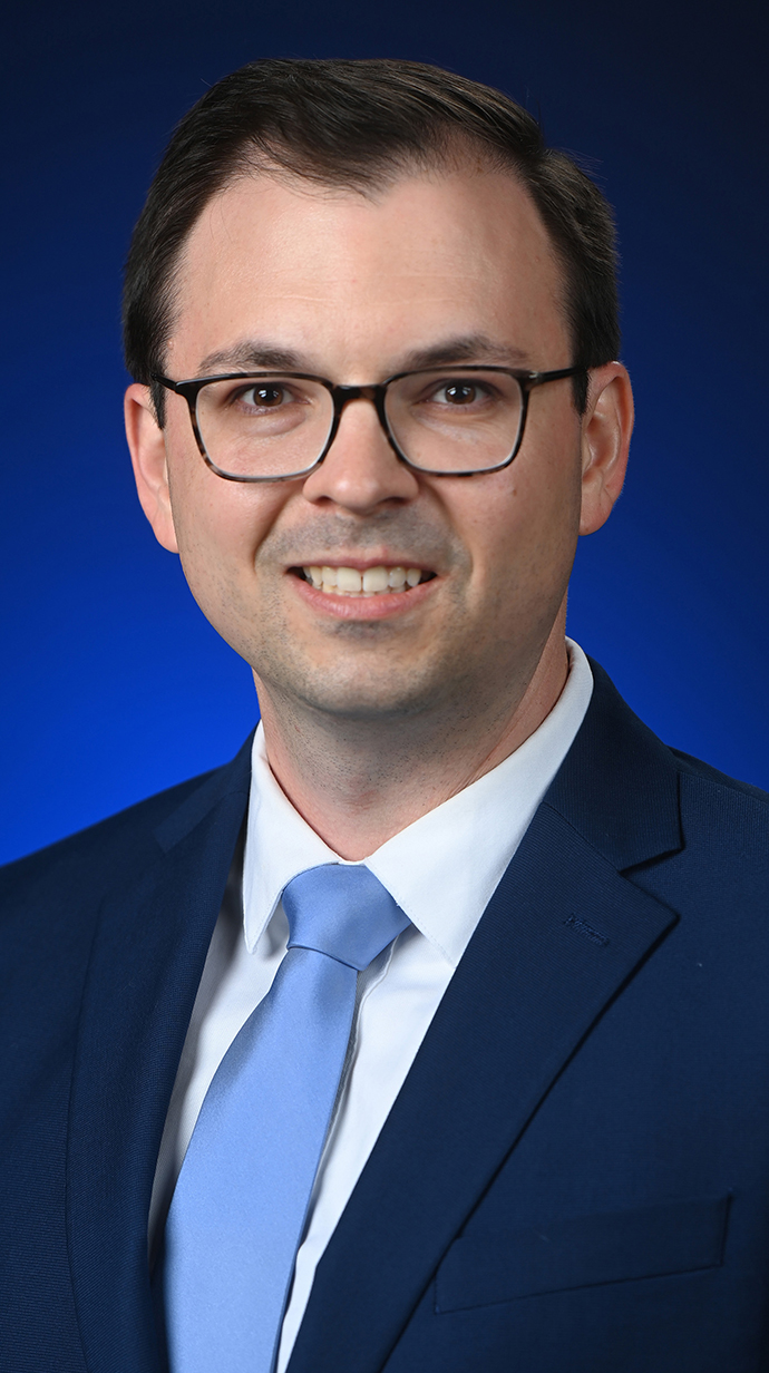 Headshot of a man wearing a dark suit with a light blue tie.