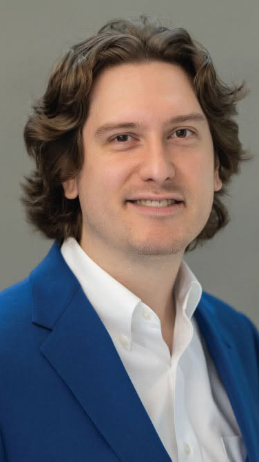 Headshot of a man wearing a blue jacket over a white open-collared shirt.