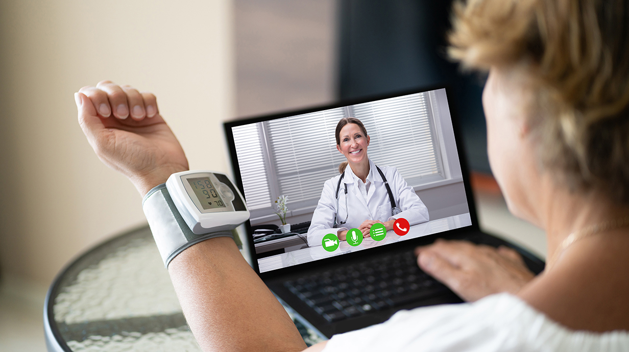 A woman wearing a blood pressure cuff talks to a doctor using a laptop computer.