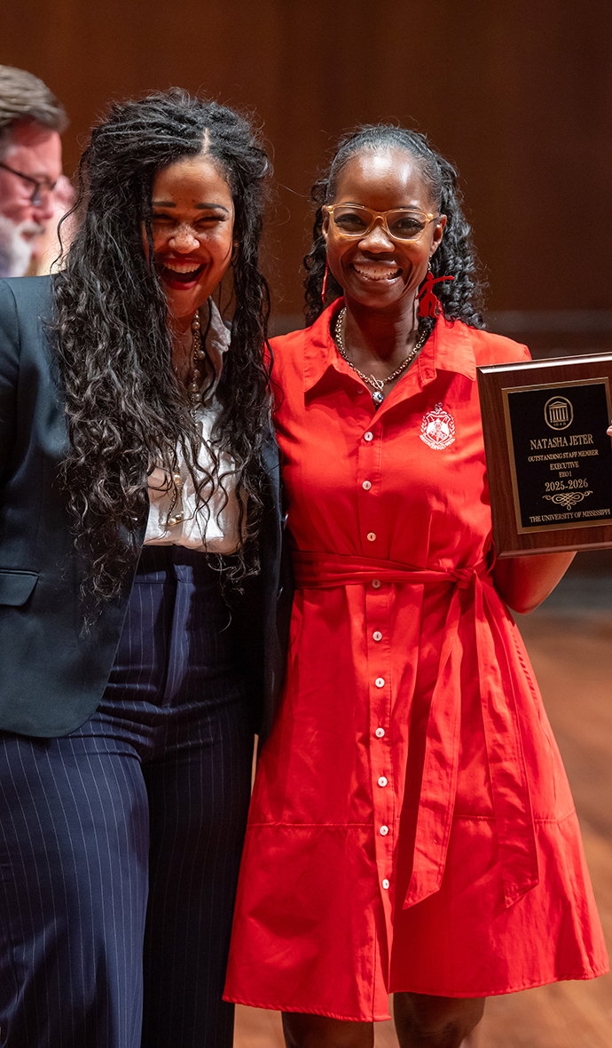 Two woman hold award plaques on a stage.