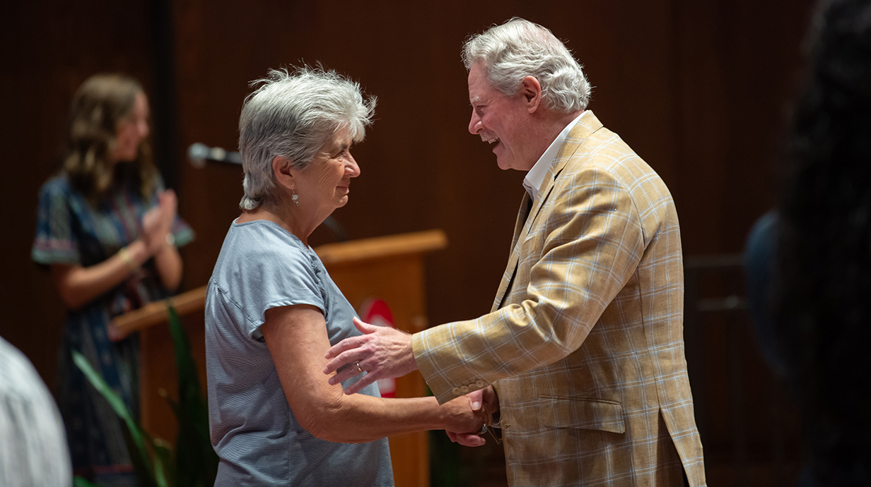 A man smiles and shakes a woman's hand on a stage.